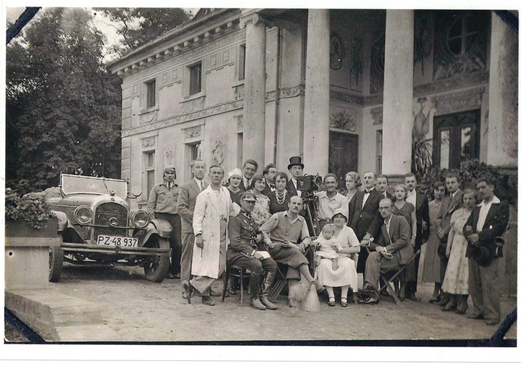 Zdjęcie przedstawiające ekipę filmową w kostiumach, przed pałacem Lipskich w Lewkowie. Pośrodku na przedzie siedzi Antonina Lipska z małym Wojciechem na kolanach